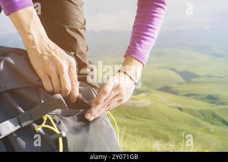 Gros plan des mains des femmes détachez la boucle sur le sac à dos du camp sur fond de la vallée dans le soleil couchant. Tourisme. Suivi Banque D'Images