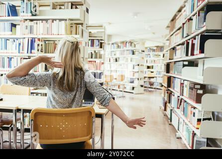 Fatigué étudiante est assis au bureau avec une pile de livres, la bibliothèque de l'université Banque D'Images