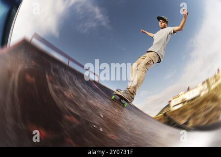 Adolescent patineur raccroché au-dessus d'une rampe sur une planche à roulettes dans un skate Park. Grand angle Banque D'Images