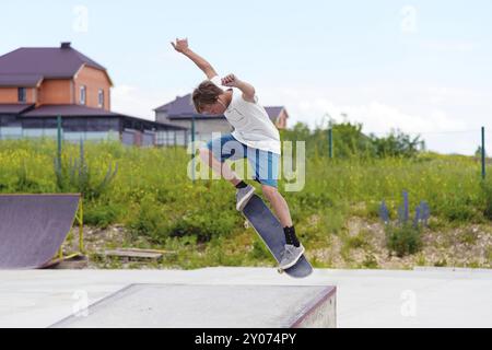 Garçon skateboarder dans un skate Park faisant un tour ollie sur un skateboard contre un ciel et des nuages d'orage Banque D'Images