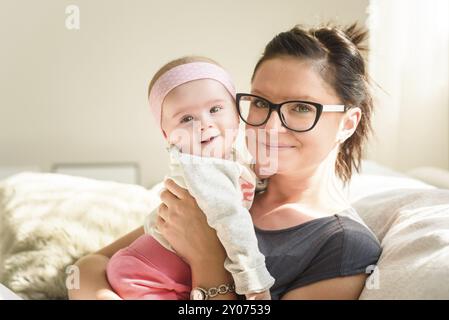 Mère tenant belle fille de bébé dans la chambre lumineuse ensoleillée. Arrière-plan de la maternité Banque D'Images