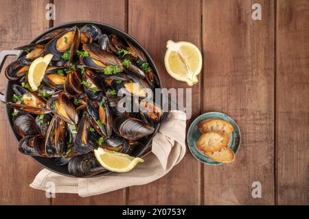 Moules marinière moules marinière,, avec du pain grillé et de tranches de citron dans une casserole, sur un top shot fond rustique en bois foncé Banque D'Images