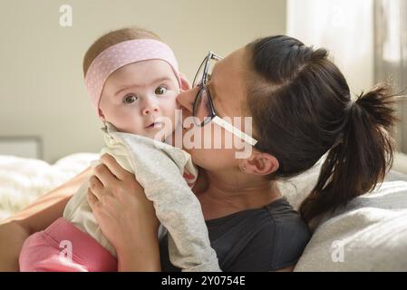 Mère tenant et embrassant belle fille de bébé dans la salle lumineuse ensoleillée. Arrière-plan de la maternité Banque D'Images