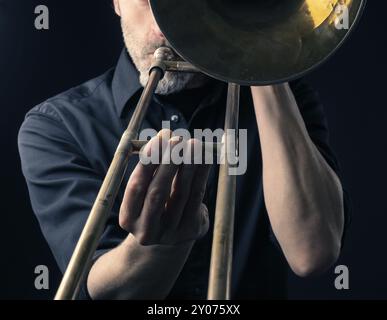 Portrait d'un musicien avec un vieux trombone poussiéreux sur fond sombre Banque D'Images