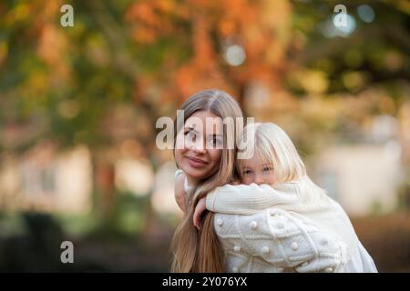 Belle jeune mère aux cheveux foncés joue avec sa petite fille de 3 ans dans le parc d'automne. Famille. Automne. Banque D'Images