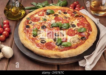 Une photo de pizza au pepperoni, avec un verre de vin blanc, huile d'olive, les feuilles de basilic, champignons, tomates cerises et, sur la pierre, sur un bac rustique foncé Banque D'Images