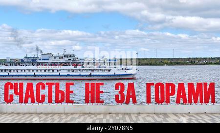 Perm, Russie - 18 mai 2024 : texte en grandes lettres russes rouges volumineuses le bonheur n'est pas loin sur le quai de la rivière Kama. Symbole de la ville de Perm. Banque D'Images