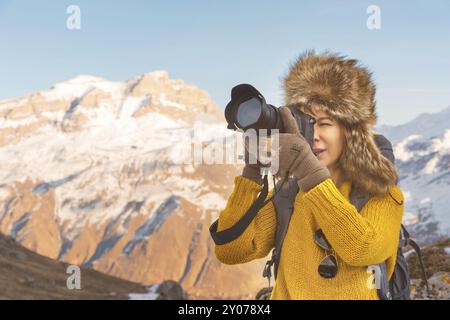 Portrait d'une fille de touriste douce dans un grand chapeau de fourrure prend des photos sur son appareil photo reflex numérique dans les montagnes. En hiver le concept de photographie dans les voyages. Banque D'Images