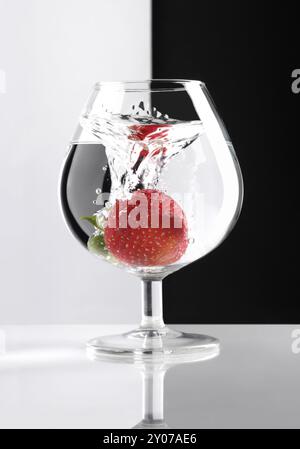 Fraise rouge trempée dans un verre de liquide clair divisé en concept artistique noir et blanc Banque D'Images