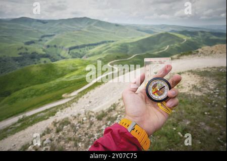 Main masculine tient une boussole magnétique sur le fond des collines et le ciel avec des nuages. Le concept de voyager et de trouver votre chemin de vie Banque D'Images