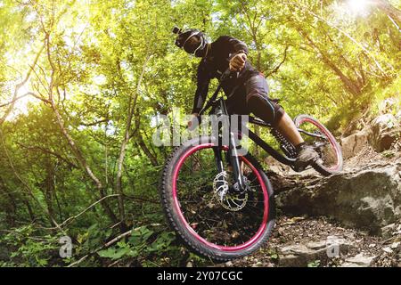 Un jeune cavalier sur un vélo pour la descente descend les rochers dans la forêt Banque D'Images