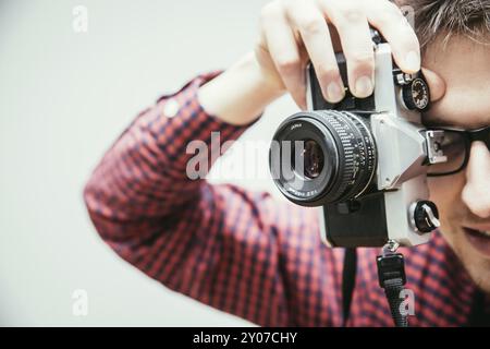 Jeune homme en chemise à carreaux rouge-bleu est de prendre une photo avec un appareil photo, vintage retro style Banque D'Images