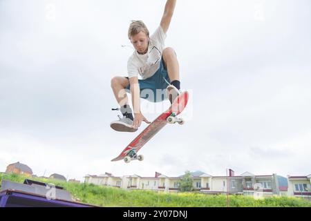 Jeune skateboarder intense en saut en hauteur contre le ciel et les zones de couchage Banque D'Images