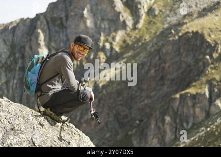 Un hipster à barbe touristique en lunettes de soleil avec un sac à dos se trouve sur le bord d'une falaise dans les montagnes près de la montagne Banque D'Images