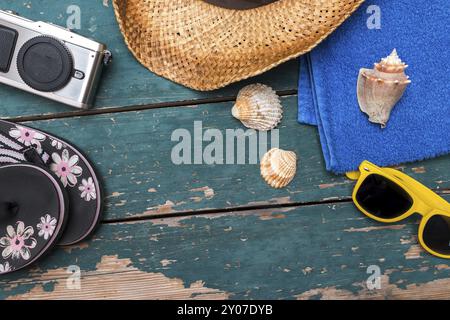 Fond d'été : concept de voyage de loisirs en été : chapeau de paille, lunettes de soleil, tongs, coquillages, appareil photo vintage et serviette de bain Banque D'Images