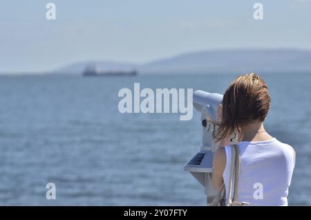 Fille à Galway à la promenade de l'océan regardant le navire sur un horizon à travers le télescope. Lieu de voyage Banque D'Images