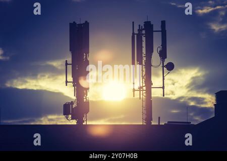 Silhouette de communication ou tour cellulaire sur le toit d'un bâtiment, soleil du soir Banque D'Images