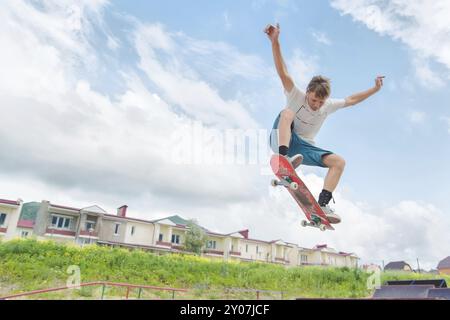 Jeune skateboarder intense en saut en hauteur contre le ciel et les zones de couchage Banque D'Images