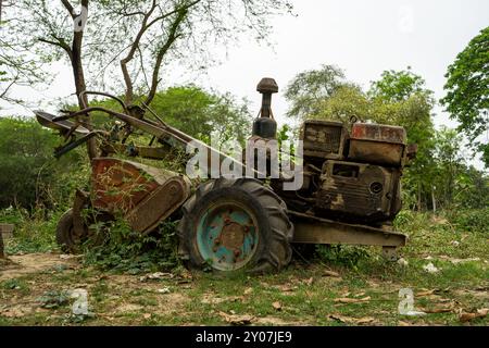 Un vieux motoculteur rouillé envahi par la végétation, abandonné dans une zone boisée avec des arbres et des arbustes en arrière-plan Banque D'Images