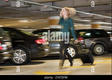 Jeune femme avec valise à roulettes dans un parking à plusieurs étages Banque D'Images