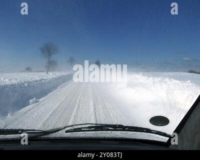 Conduite dangereuse de voiture sur route enneigée, neige flurry et mauvaise vue à travers le pare-brise, ciel bleu, espace de copie Banque D'Images