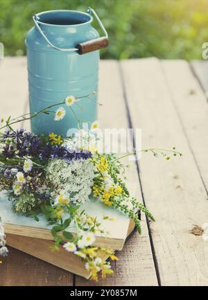 Nature morte avec fleurs près de l'arrosoir avec de vieux livres sur une table en bois rustique Banque D'Images