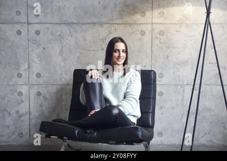 Portrait de femme brune attrayante en pull vert assis sur un fauteuil et souriant à la caméra Banque D'Images