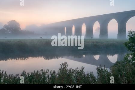 La brume couvre le paysage entourant le viaduc d'Arthington à Wharfedale, dans le Yorkshire du Nord, avec la scène reflétée dans le calme River Wharfe. Banque D'Images