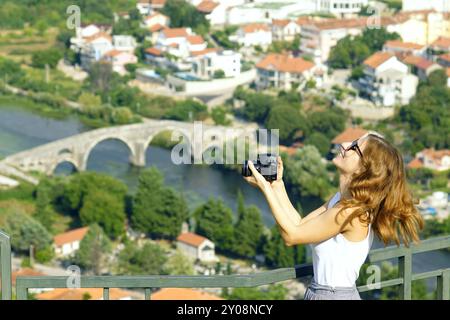 Une femme debout contre une belle vue d'un vieux pont arqué avec un appareil photo reflex numérique dans ses mains riant avec la tête jetée en arrière Banque D'Images