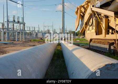 Ligne d'attaque horizontale à faible angle de deux grands poteaux électriques métalliques sur le sol. Empileuse à convoyeur jaune pour agrégats sur la droite Banque D'Images