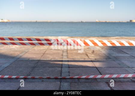 une corde rayée rouge et blanche repose sur le sol. La corde est sur une plage près de l'eau. Banque D'Images