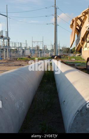 Ligne d'attaque verticale à faible angle de deux grands poteaux électriques métalliques sur le sol. Empileuse à convoyeur jaune pour agrégats sur la droite Banque D'Images