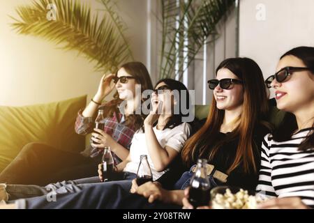 Un groupe d'amis de personnes en lunettes 3D regardent un film, souriant, riant. Manger et boire tout en regardant un film au cinéma. Les filles mangent des popc Banque D'Images