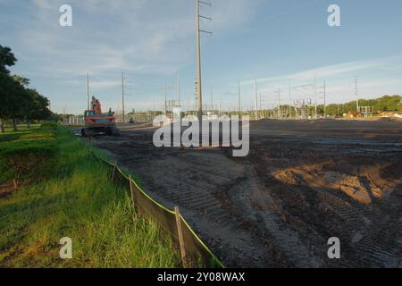 Vue large près du coucher du soleil de la sous-station électrique avec des lignes à haute puissance à Pétersbourg, Floride. Vue sur la terre, clôture temporaire en liasse, herbe verte Banque D'Images