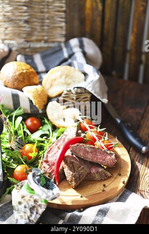 Tranches de filet de boeuf grillé à point avec faux-quartiers de pommes de terre rôties sur une planche à découper sur fond de bois Banque D'Images