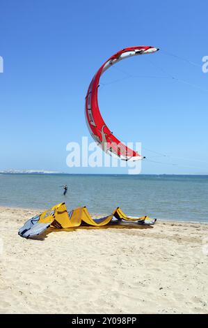 Voile rouge de kitesurfer kite surfer kite surfer debout près du spectateur dans les airs au-dessus de la plage jaune voile kite voile couché dans le sable sur la plage de sable Banque D'Images