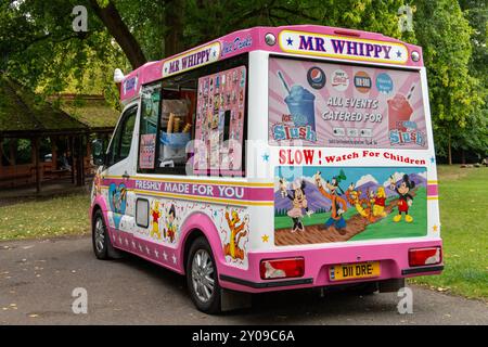 Fourgon de crème glacée coloré Mr. Whippy garé dans un parc avec diverses publicités et dessins de dessins animés, offrant des friandises fraîchement faites pour les enfants. Banque D'Images