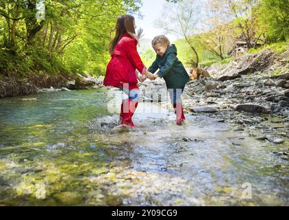 Heureux enfants portant des bottes de pluie sauter dans une rivière de montagne Banque D'Images