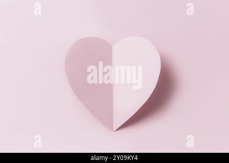 Message d'amour ou mise en place conceptuelle de Saint Valentin. Vue de dessus sur un coeur rose en papier découpé et incurvé avec ombre sur fond rose. Modèle minimaliste Banque D'Images