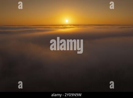 Le soleil se couche sur un horizon de nuages, projetant des teintes orange et or à travers le ciel et l'atmosphère brumeuse, Nord, Alberta, Canada, Amérique du Nord Banque D'Images