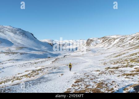 Un randonneur dans un coupe-vent jaune sur le sentier enneigé de la rivière de source chaude de Reykjadalur dans le sud de l'Islande en hiver Banque D'Images