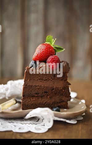 Morceau de gâteau au chocolat avec du glaçage et sur fond de bois aux petits fruits Banque D'Images