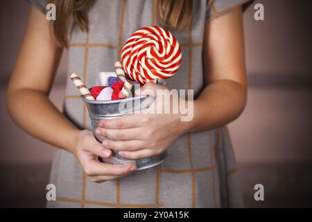 Seau avec bonbons colorés dans les mains de la petite fille. Gros plan Banque D'Images