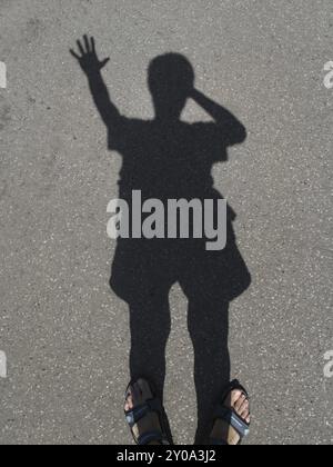 Ombre d'un homme avec une main levée sur l'asphalte gris Banque D'Images