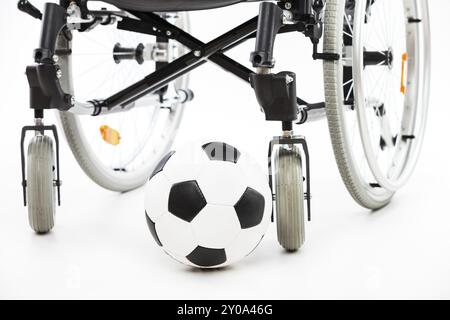 Fauteuil roulant pour personne invalide ou handicapée et ballon de football blanc isolé Banque D'Images