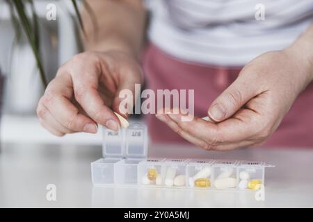 Les mains de femmes triant des pilules. Jeune femme qui reçoit ses vitamines quotidiennes à la maison. Gros plan de la boîte de pilules médicales avec des doses de comprimés pour prendre quotidiennement un médicament Banque D'Images