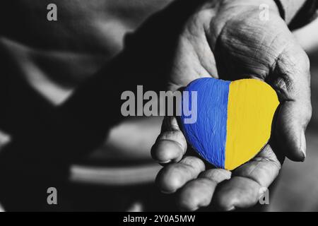 Hommes ou soldats âgés mains tenant coeur pierre peinte avec les couleurs du drapeau national de l'Ukraine. Priez pour l'Ukraine, arrêtez la guerre, sauvez le peuple d'Ukraine a Banque D'Images