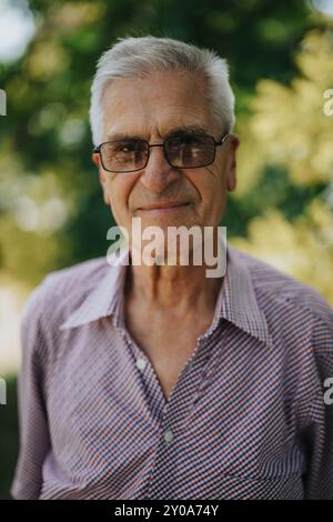 Homme âgé souriant avec des lunettes profitant d'une journée ensoleillée à l'extérieur Banque D'Images