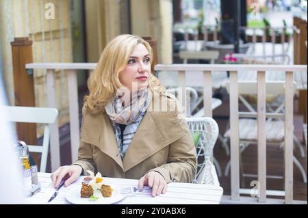 Fermez la femme blonde heureuse d'âge moyen dans le café en plein air regardant dans la distance Banque D'Images