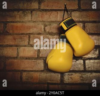 Paire de gants de boxe jaune accroché sur un mur de briques Banque D'Images